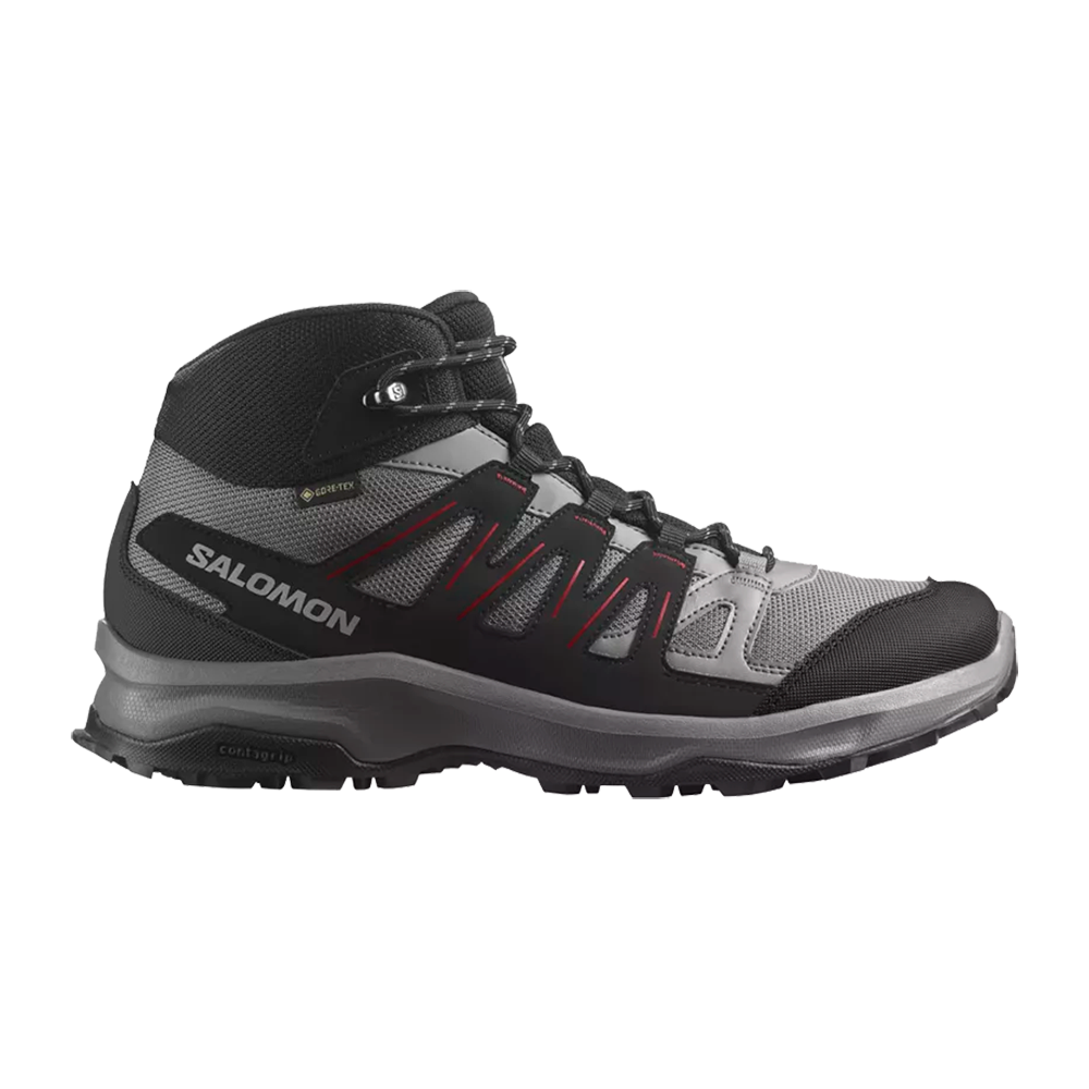 Dette billede viser en Salomon vandrestøvle i grå og sort med røde detaljer. Støvlen har et mellemstort skaft for god ankelsupport, åndbart mesh og forstærkede syntetiske overlays for beskyttelse. Gore‑Tex-mærket antyder vandtætning, mens den robuste sål med dybe mønstre giver godt greb på ujævnt terræn. Designet balancerer komfort, holdbarhed og stabilitet til længere ture.