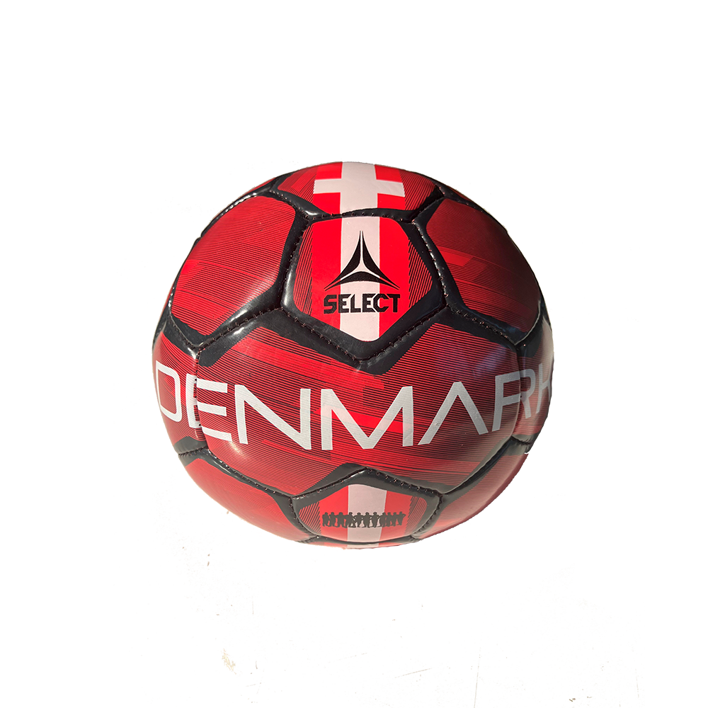 Bolden er en rød og sort sportsbold med tydelig tekst "DENMARK" og mærket "Select" i midten. Den har et mønster af sammenføjede paneler og et hvidt kors øverst, der refererer til Dannebrog. Overfladen er let struktureret, og farverne giver et energisk og nationalt udtryk. Skyggen på underlaget antyder, at bolden ligger på en lys flade i klart lys.