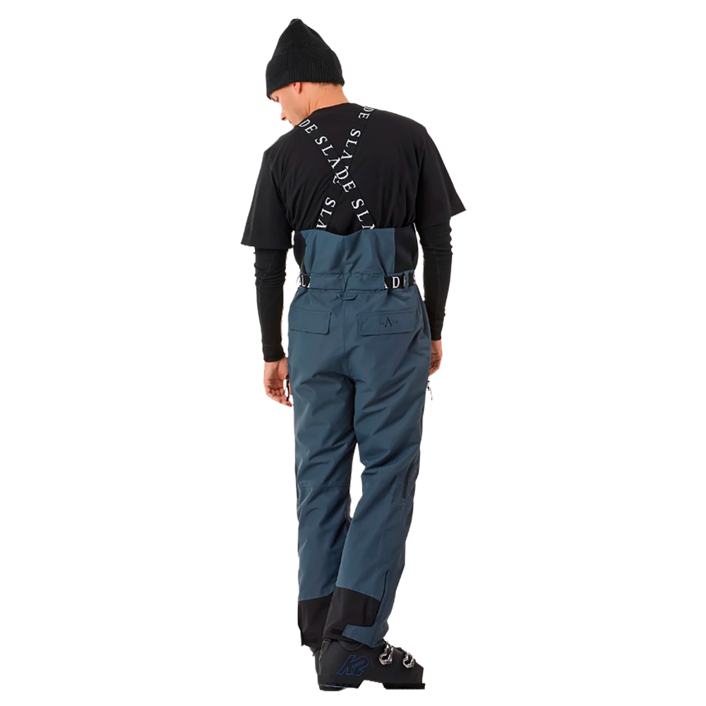 På billedet ses en mand iført Slade Aspen Bib Pants - Herre Skibukser fra mærket Slade. Bukserne har en dyb blå farve og er designet til at yde maksimal komfort og funktionalitet under skisport. De er udstyret med justerbare seler og flere funktionslommer, hvilket gør dem ideelle til både professionelle og amatørsportere. Stil og praktik går hånd i hånd med disse højkvalitets skibukser.