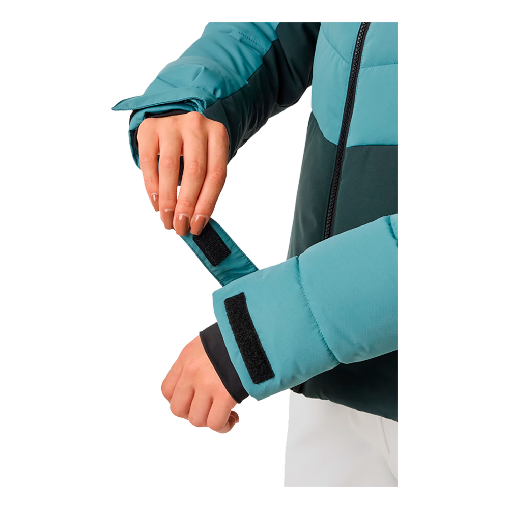 Billedet viser en model iført Swedemount Vail Ski Jacket W, en dameskijakke designet til kølige dage på skibakkerne. Jakken, som har flotte farver i slående turkis og mørkegrønt, fremhæver en kombination af funktionalitet og moderigtig stil. Den funktionelle design inkluderer en hætte, flere lommer og en justerbar pasform. Jakken ser ikke alene varm og behagelig ud, men også ideel til vintersportsgrene, hvilket tilføjer en smart og praktisk løsning til enhver vintergarderobe.