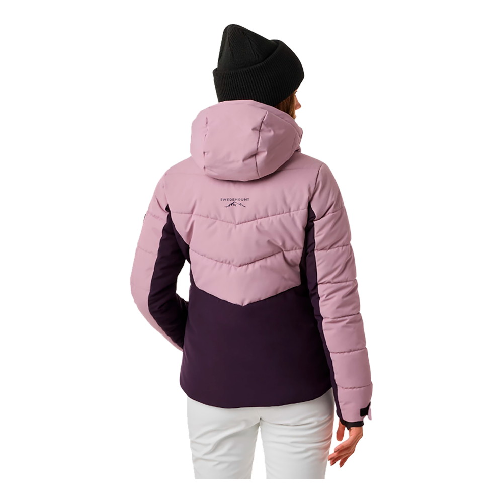 Denne billede viser en kvinde iført Swedemount Vail Ski Jacket W, en skijakke designet specifikt til damer. Jakken har en tiltalende farvekombination med lyserød på øvre del og mørkeviolet på den nedre del. Jakken er udstyret med en justerbar hætte og praktiske lynlåslommer, der gør den både stilfuld og funktionel. Det tydelige Swedemount logo på hætten tilføjer et sporty touch. Jakken ser ud til at være ideel til både skiture og daglig brug i vintermånederne.