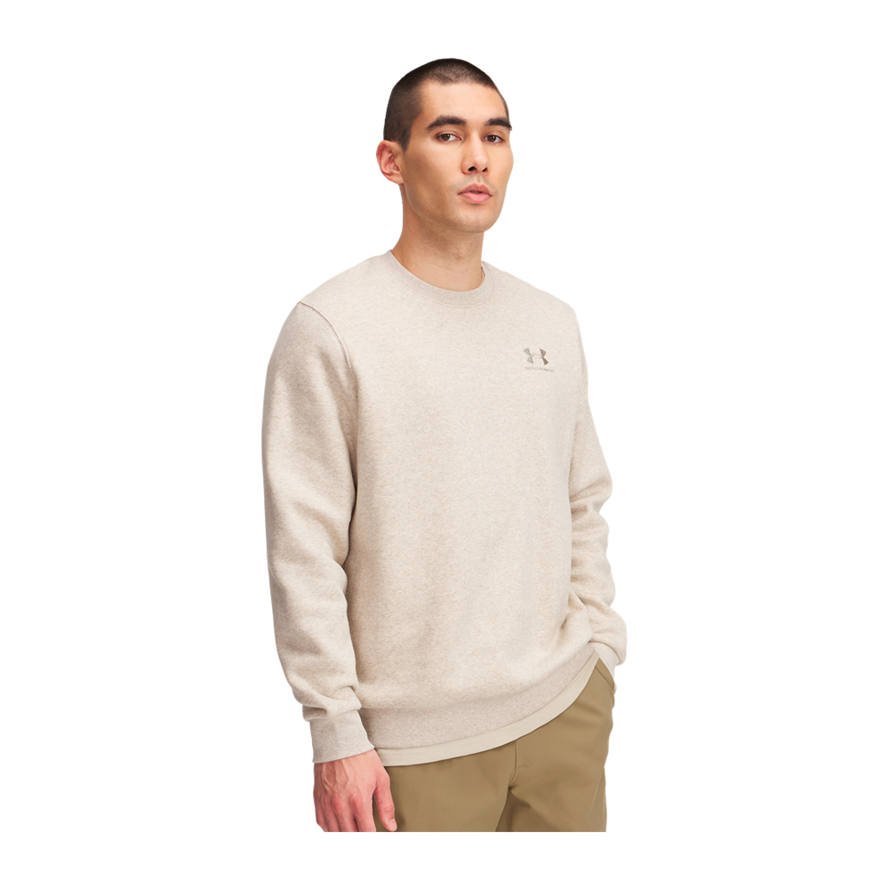 En ung mand står i trekvart profil iført en enkel, lys beige sweatshirt med et diskret logo på venstre bryst. Han har kortklippet hår og et afslappet, roligt udtryk, hånden i lommen og kroppen let vendt til siden. Bukserne er khaki, og billedet signalerer et minimalistisk, hverdagsagtigt og behageligt look med fokus på komfort og enkel stil.