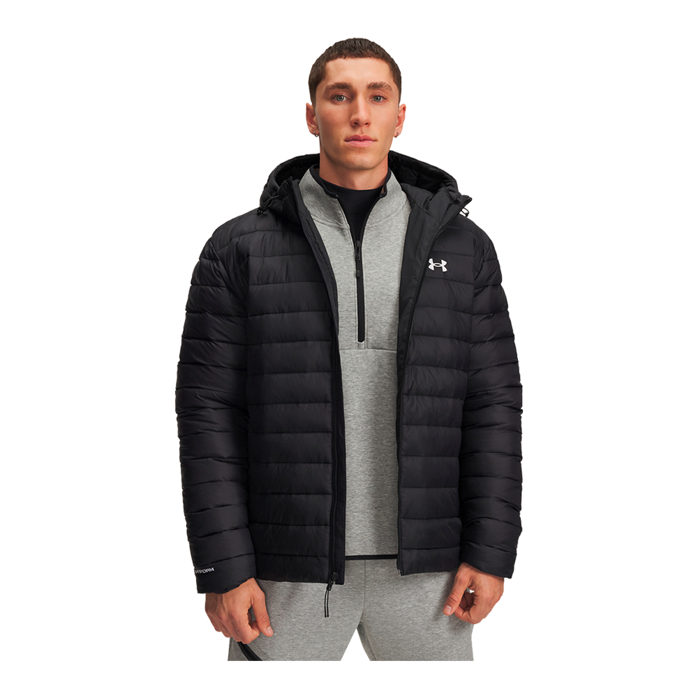 En ung mand iført en sort, letvægts-dunjakke med hætte står afslappet og kigger fremad. Under jakken ses en lysegrå, zip-up sweatshirt og matchende træningsbukser, hvilket giver et sporty og funktionelt look. Jakken har vandafvisende struktur og et diskret logo på brystet. Motivets neutrale udtryk og rene linjer fremhæver et minimalistisk, praktisk outfit til kølige dage.