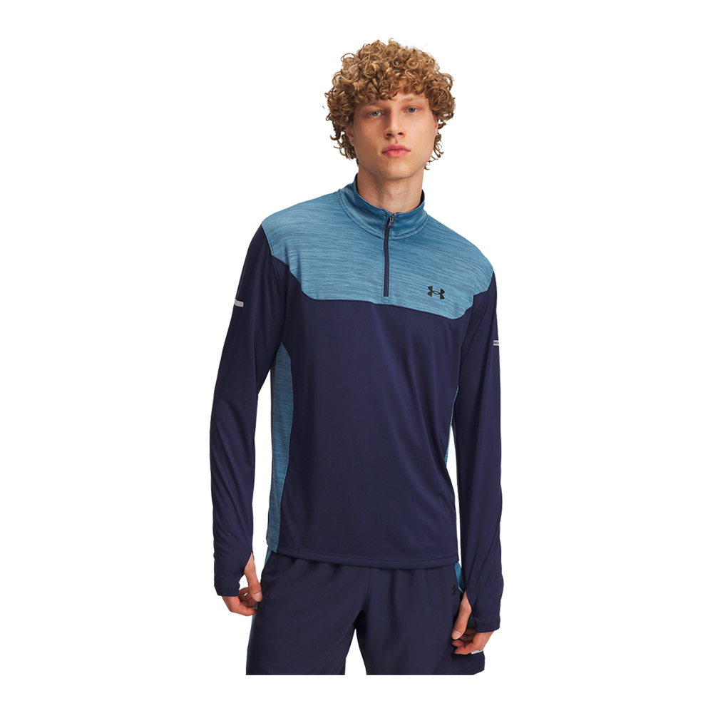 En ung mand iført en sporty langærmet træningsoverdel i to nuancer af blå — mørk navy som hovedfarve og lysere meleret blå øverst og i siderne. Trøjen har en kort lynlås ved halsen, tætsiddende pasform og svedtransporterende materiale, hvilket giver et funktionelt, moderne look. Modellen står afslappet med hænderne ned langs kroppen og et neutralt, fokuseret udtryk.