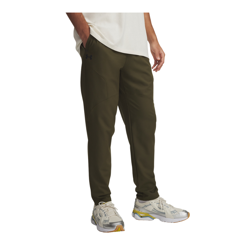 Mand iført olivengrønne, smalle træningsbukser med tapede syninger og diskret logo ved hoften. Bukserne er lavet i blødt, teknisk materiale med skrå lommer, og har en tætsiddende, tapered pasform der samler sig ved anklen. Han har en hvid t-shirt og hænderne halvt i lommerne, kombineret med hvide sneakers med grå og gule detaljer — et afslappet, sporty hverdagslook.