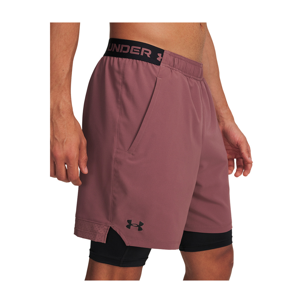 mauve med en sort, integreret compression-underdel. Ydershortsen har elastisk linning med synlig "Under" tekst, sidelommer og en lille Under Armour-logo ved venstre benkant. Materialet virker let og åndbart med små slidser i siderne for bevægelsesfrihed. Designet passer til løb, gym og andre aktive aktiviteter.