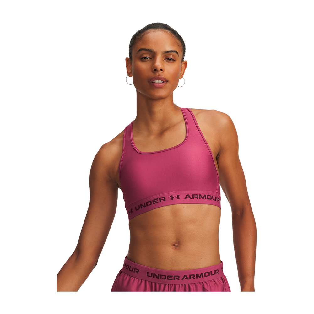 magenta sports-bh og matchende shorts fra Under Armour. Hun står selvsikkert med opstrammet hår i en knold, bærer store øreringe og har en tonet overkrop. Farverne er klare og sporty, og tøjet har synligt logo ved kanten. Stemningen er energisk og fokuseret, egnet til træning eller activewear-markedsføring.