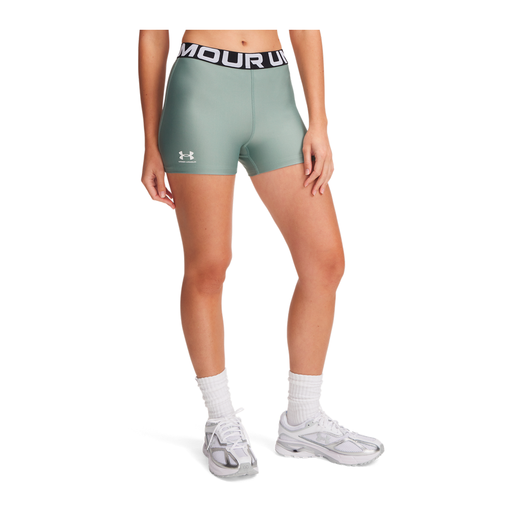 En person står i et par tætsiddende, salviegrønne træningsshorts fra Under Armour med sort elastisk linning og hvidt logo på låret. Shortsene sidder højt i taljen og fremhæver benenes muskulatur. Modellen bærer hvide mellemlange træningssokker og sneakers i hvidt med grå detaljer, hvilket giver et rent og sporty udtryk velegnet til fitness eller løb.