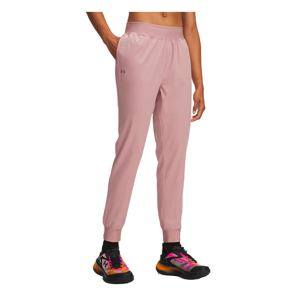 Billedet viser en sporty, afslappet stil med lyserøde træningsbukser i et blødt, let materiale. Bukserne har høj talje med bred elastik, sidelommer hvor hånden er anbragt, samt ribkant ved anklerne for en tætsiddende pasform. Et diskret logo pryder låret. Kombinationen med farverige løbesko i pink, orange og sort giver et energisk, moderne look velegnet til både træning og afslappet hverdag.