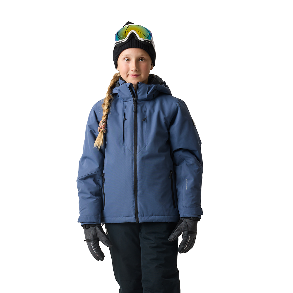 En ung pige står afslappet mod en neutral baggrund iført en varm, blå skijakke med hætte, mørke skibukser og isolerede handsker. Hun har en sort hue med skibriller placeret ovenpå og et langt flet hår trukket over skulderen. Jakken har lynlåse i siderne og et rent, funktionelt snit, der signalerer praktisk og vinterklar påklædning til udendørsaktiviteter i koldt vejr.