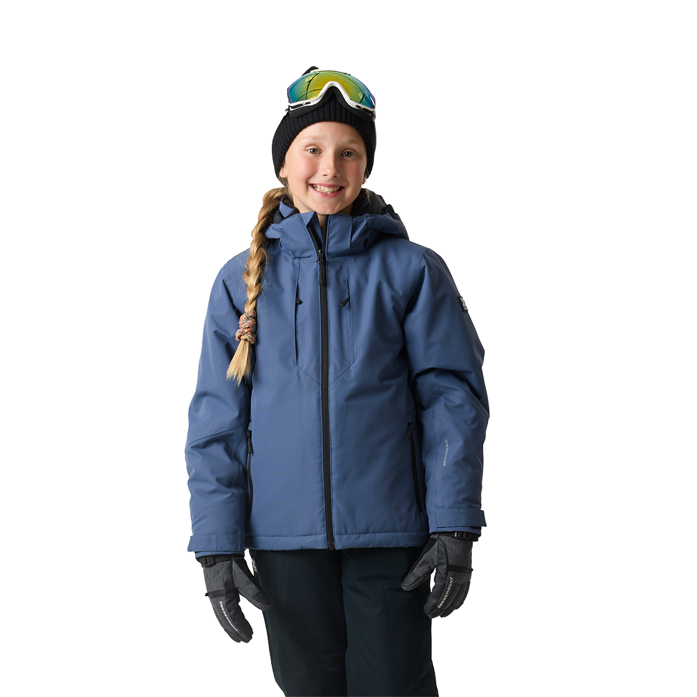 Et smilende barn iført teknisk skijakke i blå, mørke skibukser og varme handsker står klar til vinteraktiviteter. Hovedet er dækket af en sort hue, og skibrillerne er placeret ovenpå huen. Håret er flettet til siden. Jakken har høj krave og lynlås foran, og hele udstyret signalerer funktionel, komfortabel beklædning til koldt vejr og sne.