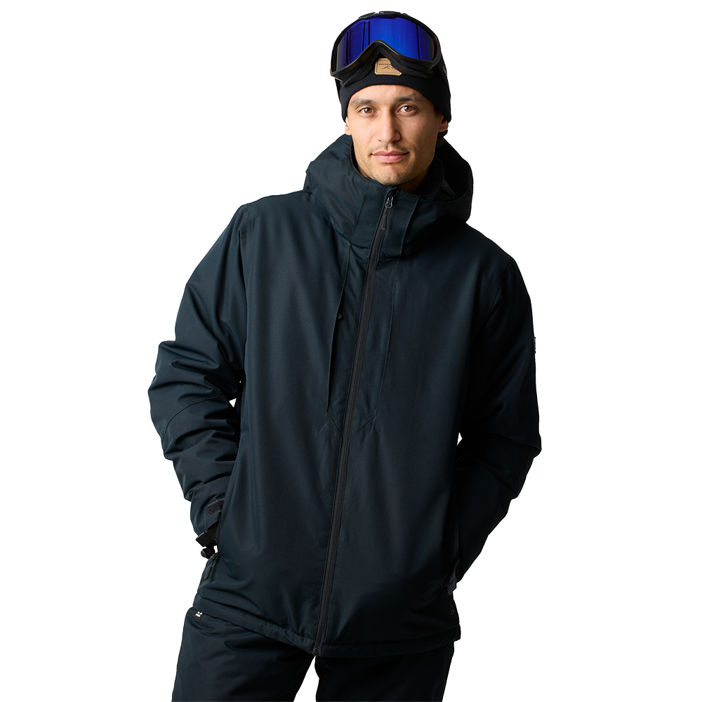 En mand iført en mørk, vandtæt skijakke med høj krave og hætte ser roligt mod kameraet. Han bærer en sort beanie og har skibriller med blåt spejlglas placeret over panden. Jakken er praktisk og isolerende med lynlås og sidelommer, og hans hænder er gemt i lommerne. Det neutrale, lyse baggrund fremhæver tøjets funktionelle og stilrene udtryk.