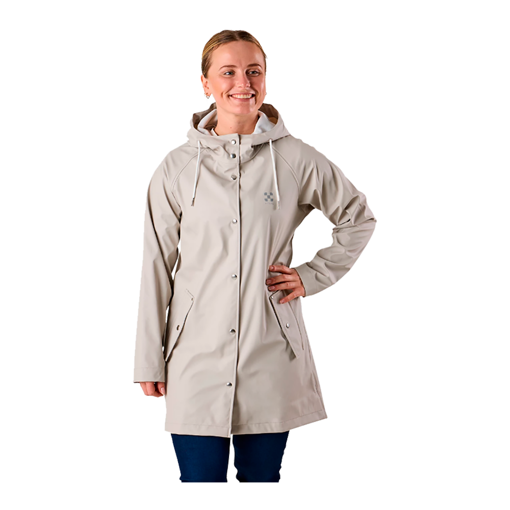 En kvinde står i en afslappet, opretstående stilling og smiler varmt. Hun bærer en lys beige regnjakke med hætte og trykknapper, lommer foran og snore ved kraven. Jakken går til midt på låret og er kombineret med mørke bukser. Hendes ene hånd hviler i siden, hvilket giver et selvsikkert og afslappet udtryk, velegnet til hverdag og regnvejr.