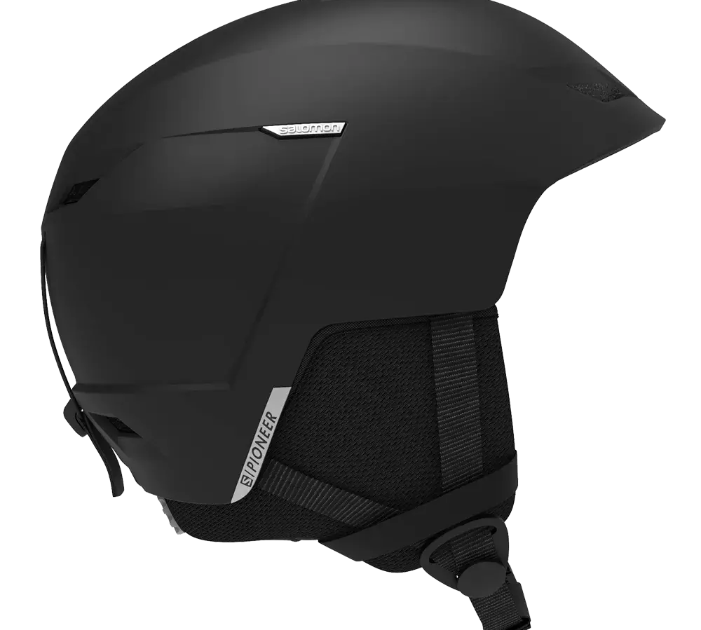 En slank, mat sort skihjelm med moderne, aerodynamisk form og diskrete logoer ("Salomon" og "Pioneer"). Hjelmen har bløde ørepolstre, ventilation i skallen og et justerbart hageremssystem med spænde. Overfladen er enkel og robust med minimale detaljer, designet til både komfort og sikkerhed i koldt vejr. Den fremstår let, praktisk og velegnet til alpine aktiviteter og fritidsski.