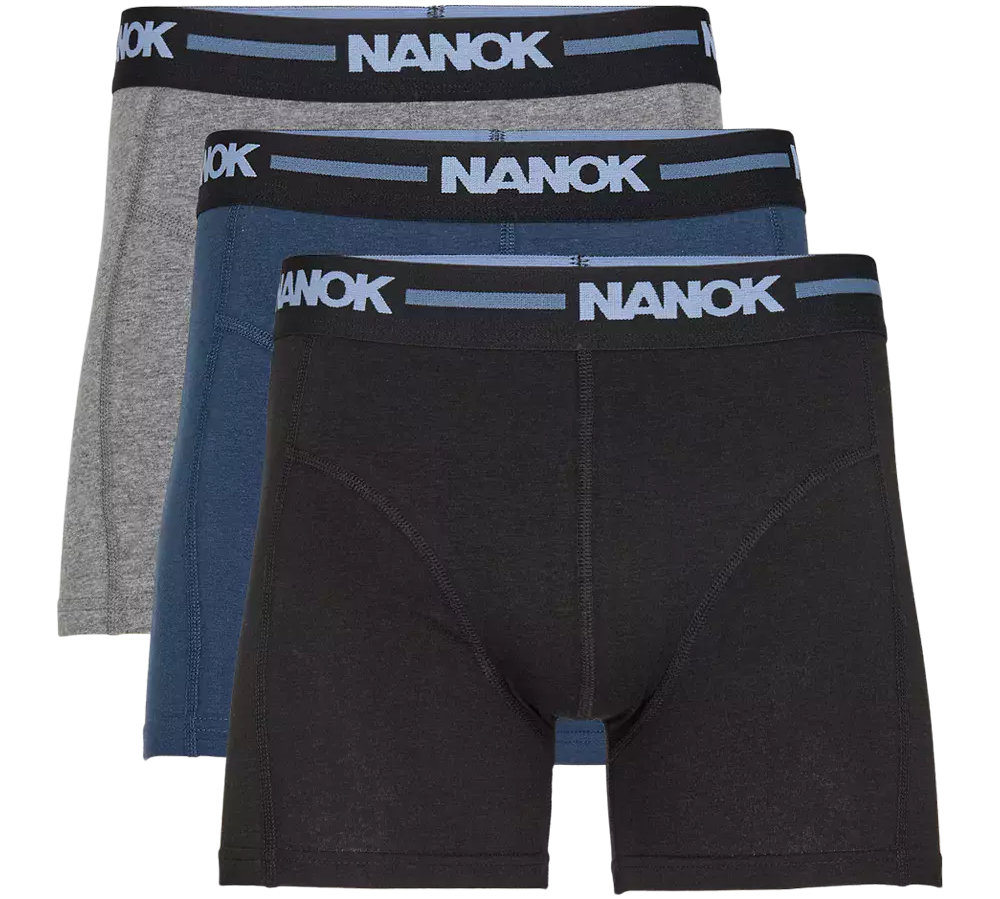 Et sæt tre boxershorts i klassisk, minimalistisk design: én sort, én blå og én grå. Hver har bredt, elastisk taljebånd i sort med lyseblåt "NANOK"-logo, flade syninger og en tætsiddende, støttegivende pasform. Materialet fremstår blødt og fleksibelt, ideelt til hverdag eller sport. Enkel farvepalet og diskret branding gør dem lette at matche med forskellige outfits.
