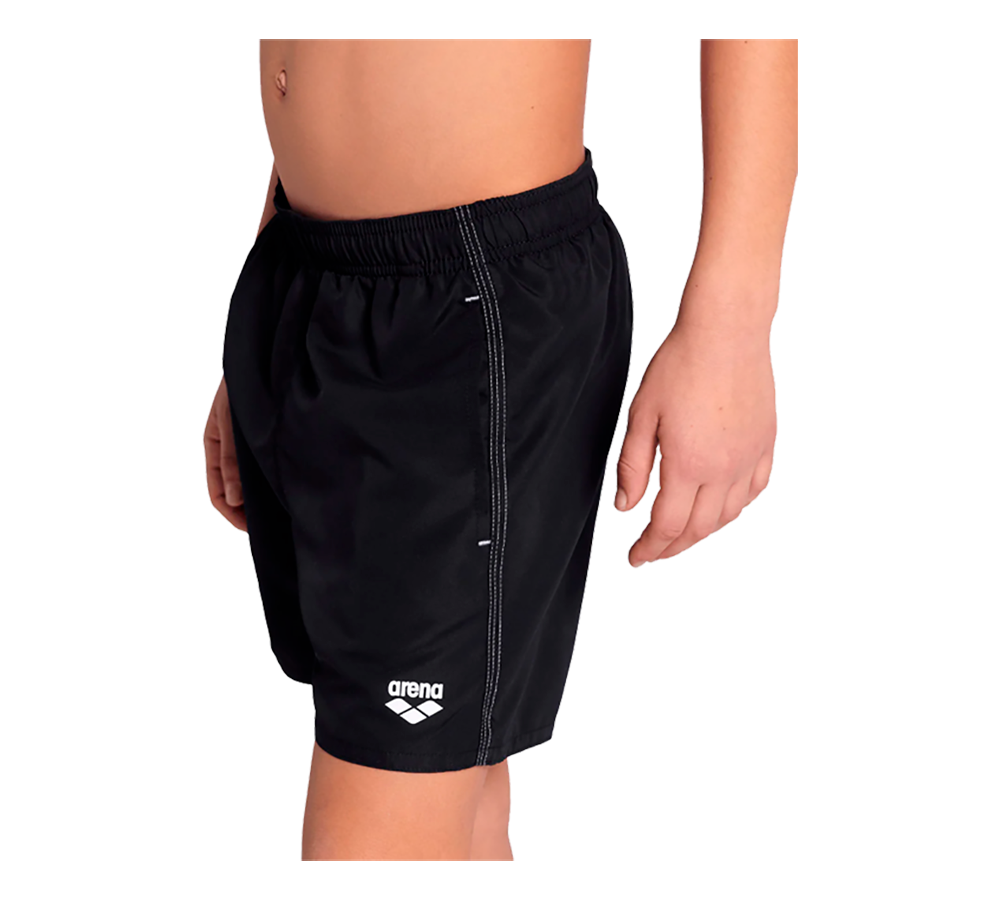 Billedet viser en ung person iført sorte badeshorts fra Arena. Shortsene har elastisk talje, knælængde pasform og et lille hvidt logo nederst på venstre ben. Siderne har synlige kontrastsømme og en enkel, sporty silhuet. Materialet virker let og hurtigtørrende, velegnet til svømning eller strandbrug. Farven er klassisk sort, hvilket giver et tidløst og neutralt udtryk.