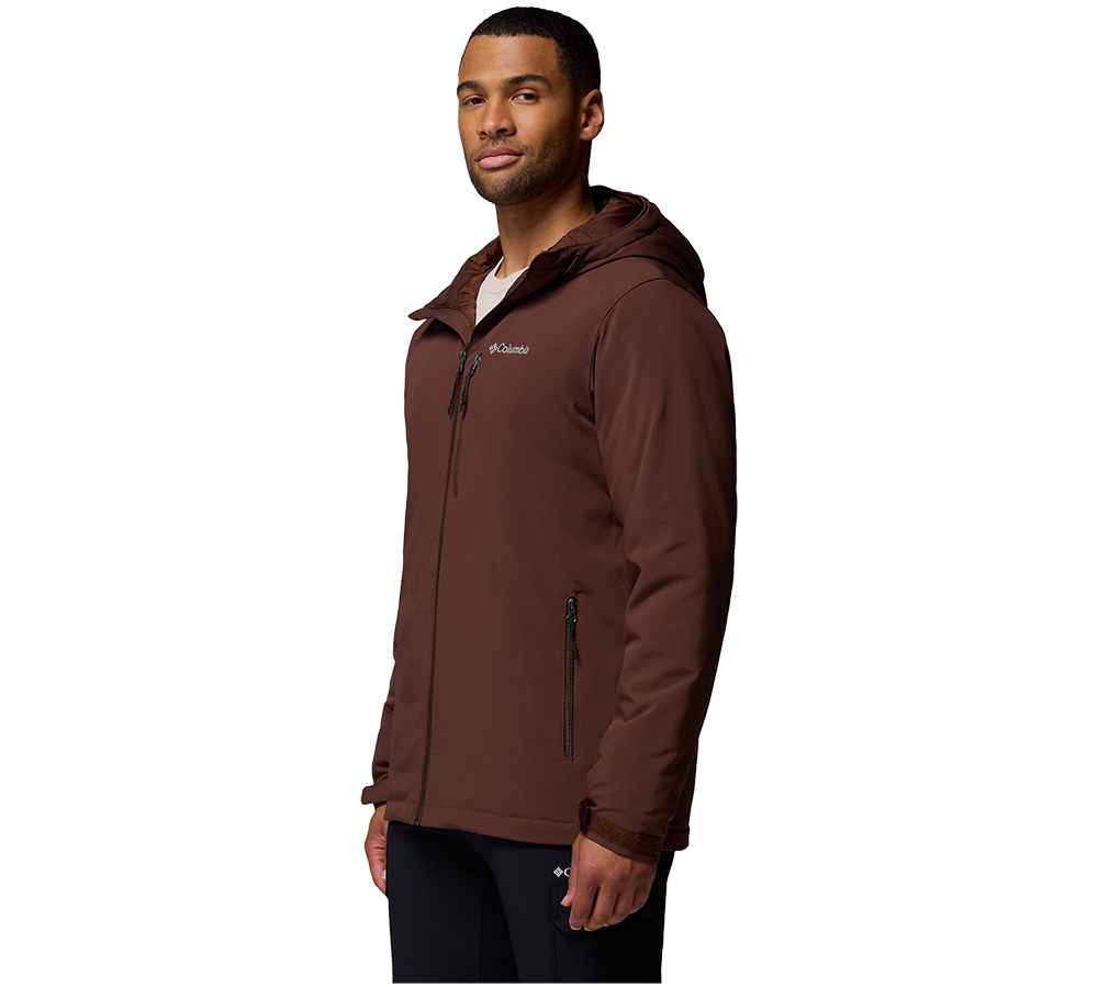 Et portræt viser en mand i trekvart profil iført en brun, vandafvisende softshell-jakke med hætte. Jakken har synlig lynlås, lommer med lynlås og et diskret logo på brystet. Han står afslappet med hænderne ned langs siden og bærer mørke bukser. Billedet er taget mod en neutral, hvid baggrund og fremhæver jakkeens rene linjer og funktionelle detaljer.