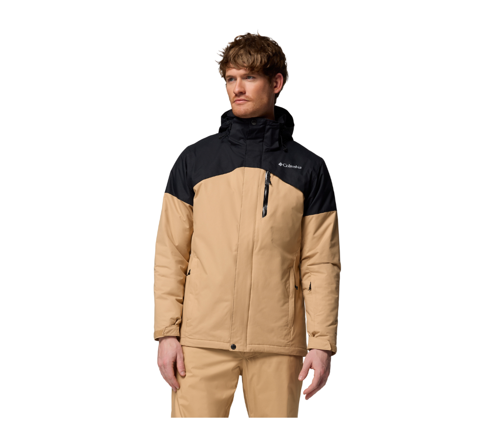 En ung mand står iført en tofarvet Columbia-jakke i beige og sort med hætte. Jakken har en vandtæt lynlåslomme på brystet, sidelommer og en justerbar krave, hvilket giver et robust og funktionelt udtryk. Han ser afslappet til siden, og tøjet virker velegnet til koldt eller vådt vejr, kombineret med matchende beige bukser for et praktisk outdoor-look.
