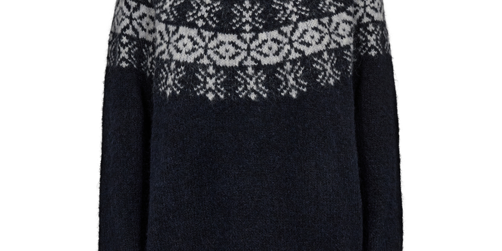 Mørkeblå, kraftig striktrøje med traditionelle nordiske mønstre i hvidt tværs over bryst og skuldre. Høj ribstrikket krave, lange ærmer og ribkant forneden. Garnet virker blødt og let ludet, som mohair eller uld, hvilket giver et varmt og hyggeligt udtryk. Enkel, klassisk pasform der egner sig godt til vinterbrug og afslappede lag-på-lag looks.