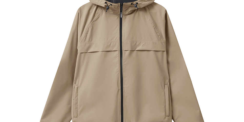 En stilren, beige regnjakke med hætte og sort tovejslynlås i midten. Jakken har en enkel, minimalistisk silhuet med diskrete sidelommer, elastiske ærmekanter og en justerbar hætte med snore. Materialet virker vandafvisende og let, ideel til byliv og udendørs aktiviteter på vådt vejr. Farven er neutral og alsidig, hvilket gør jakken nem at kombinere med både hverdagstøj og aktive outfits.