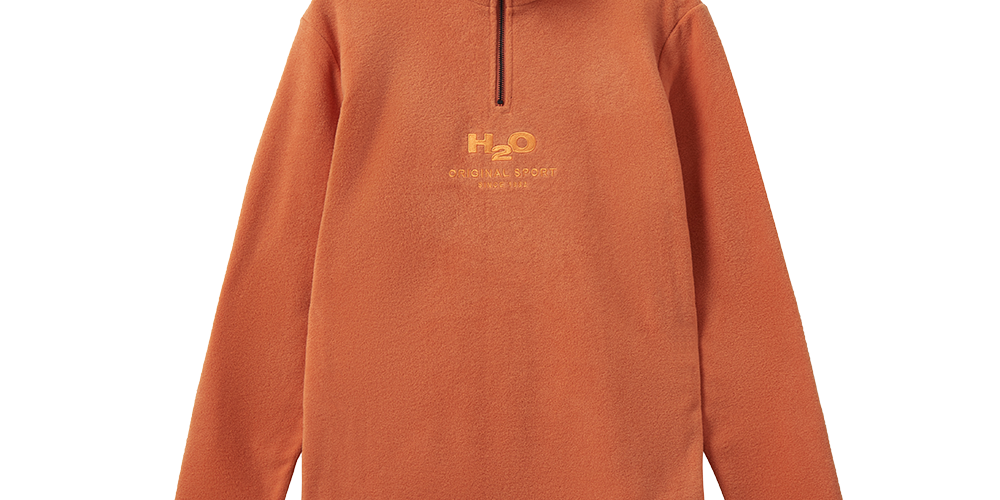En varm, brændt orange fleece-trøje med høj krave og kort sort lynlås i halsen. Simpelt og funktionelt snit med lange ærmer og ribdetaljer ved kant og ærmer. Broderet H2O-logo og teksten "Original Sport" midt på brystet giver et sporty udtryk. Materialet føles blødt og isolerende. Ideelt til efterår og vinter som mellemlag eller til afslappet, aktivt hverdagsbrug.