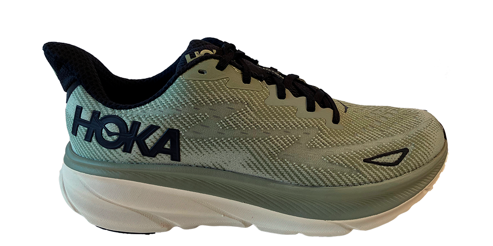 Billedet viser en moderne løbesko fra HOKA i afdæmpet grøn med sort snørebånd og mørk inderforing. Skoen har en markant, tyk mellemsål i lysegrøn og hvid, der signalerer god støddæmpning og komfort. Den lette mesh-overdel har struktureret mønster og logo på siden. Designet kombinerer funktionalitet og æstetik, velegnet til lange træningspas og daglig løbetræning.