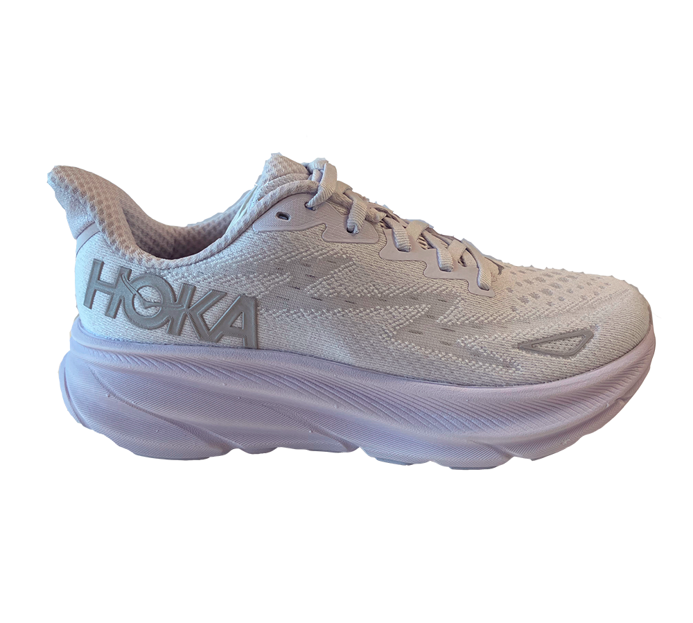 En lyslilla og hvid løbesko fra HOKA ses i profil. Skoen har en luftig, strikket mesh-overdel, traditionelle snørebånd og et tydeligt HOKA-logo på hælen. Den markante, ekstra polstrede mellemsål er buet og giver et støddæmpende, cushioned udtryk. Designet kombinerer funktionel komfort med moderne æstetik — velegnet til lange løbeture eller hverdagsbrug, hvor støtte og affjedring prioriteres. Den føles let på foden med diskrete forstærkninger ved tåen.