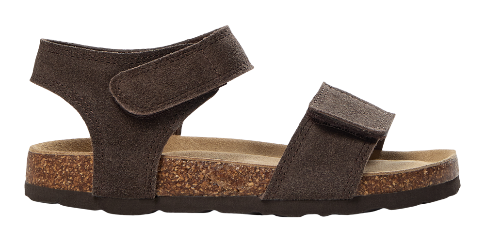 Brun sandal i ruskind med to brede velcro-remme over forfoden og om anklen. Indersålen er formstøbt med blødt, lysebrunt indlæg, og mellemsålen er lavet af kork med synlig tekstur, mens ydersålen er mørk gummi. Designet er enkelt og funktionelt, egnet til afslappet hverdag og varme dage, hvor komfort og justerbar pasform prioriteres.