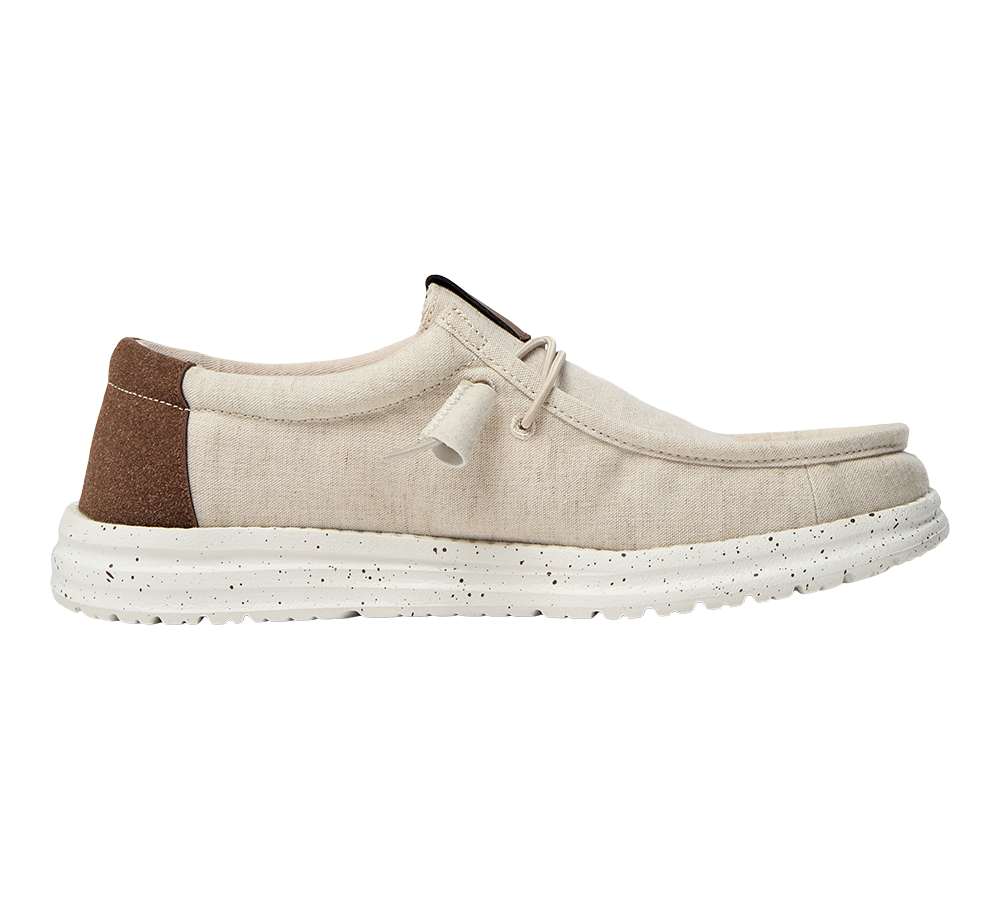 Et lyst, casual lærredssko set fra siden med en enkel, lav profil. Overdelen er beige canvas med synlige syninger og en brun ruskindsforstærkning ved hælen. Skoen har en afslappet moccasinform, korte snørebånd med knude og en tyk, hvid gummisål med sorte prikker, der giver et moderne, råt touch. Perfekt til afslappet hverdag og sommerbrug.