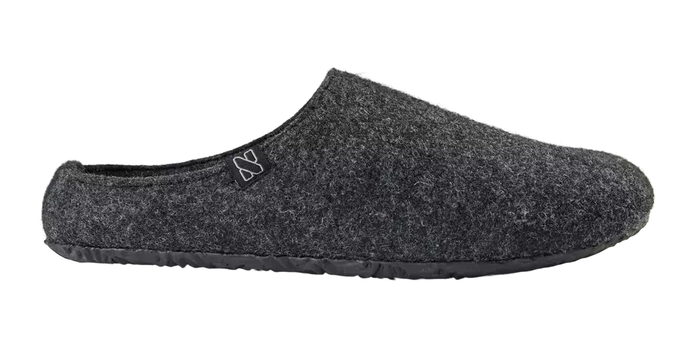 En enkel, mørkegrå hjemmesko i filtet uld med åben hælkappe og skridsikker gummisål. Den mule-formede sko har et minimalistisk, nordisk design og et lille logo ved åbningen. Den bløde, tætte filt giver varme og komfort til kolde fødder, mens den faste sål gør den velegnet til korte ture udendørs. Perfekt til afslapning derhjemme eller som praktisk indendørs fodtøj.