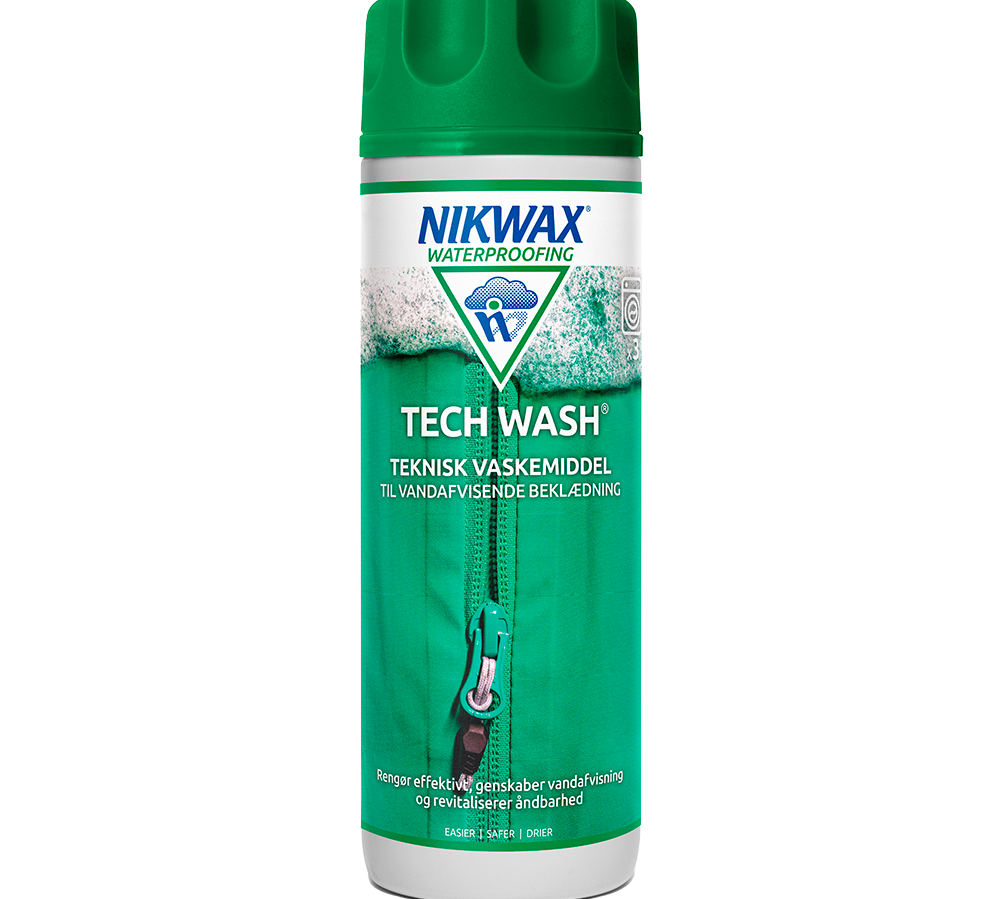 Et billede af en Nikwax Tech Wash-flaske: høj, cylinderformet beholder med grønt låg og tydelig grøn-hvid label. Produktnavn og logo fremgår klart, samt teksten "teknisk vaskemiddel til vandafvisende beklædning". Designet viser en lynlås og skum, der signalerer rengøring og genoplivning af imprægnering. Produktet markedsføres til at rense, genskabe vandafvisning og bevare stofs åndbarhed ved udendørs beklædning.