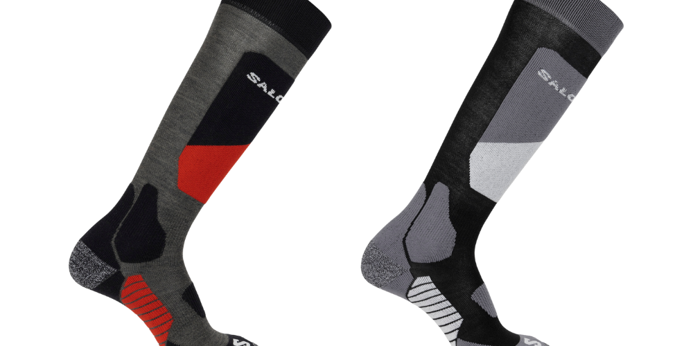 To par tekniske, knælange sokker er vist mod sort baggrund. Den ene sokke kombinerer grå, sort og røde paneler med forstærket hæl og tå samt ribstrik ved svangen. Den anden er i toner af sort og grå med lysere geometriske felter og lignende pudede zoner for komfort og støtte. Begge sokker har en sportslig, anatomisk pasform egnet til udendørs aktiviteter.