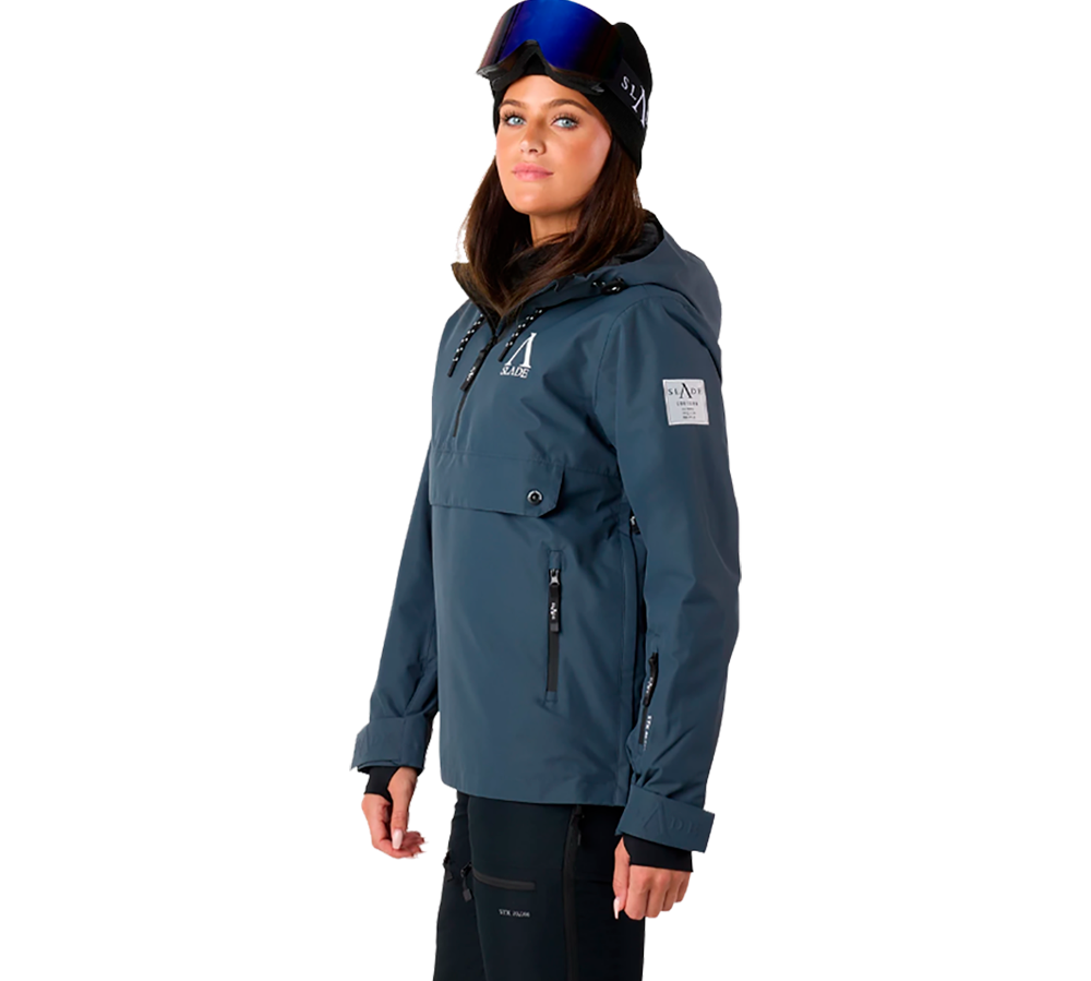 Denne billede viser en model klædt i "Slade Aspen Anorak W" fra Slade, designet til damer. Anorakken er i en stilfuld blå farvetone og fremstår med rene linjer og minimalistiske detaljer. Modellen bærer også en matchende skihjelm, hvilket antyder anorakkens anvendelse i vinter sportsgrene. Der er flere synlige lommer, der både er praktiske og bidrager til det moderne look. Dette beklædningsstykke kombinerer funktionalitet med en trendy æstetik, perfekt til aktiv brug i kølige omgivelser.