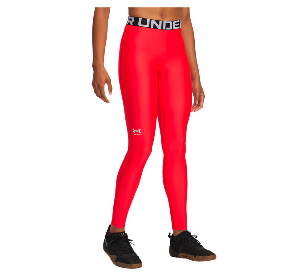 En model bærer et par skinnende, højttaljede træningsleggings i intens rød farve med en bred, sort elastik i taljen markeret af "UNDER ARMOUR"-tekst. Leggingsene har tæt, kropsnær pasform og et lille hvidt logo på låret. Kombinationen med sorte træningssneakers giver et sporty, funktionelt udtryk, velegnet til fitness, løb eller hverdagsaktiviteter, hvor bevægelsesfrihed og synlig stil prioriteres.