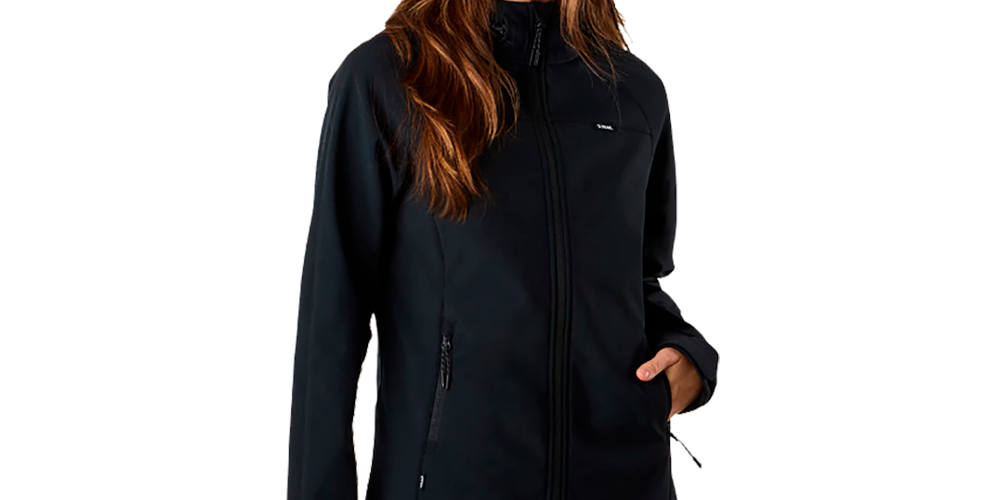 En ung kvinde står afslappet i en mørk, tætsiddende softshell-jakke med lynlås, hævet krave og lommer. Hendes langt, bølget hår falder over skuldrene, og hun kigger blidt mod siden med et roligt smil. Hun bærer mørkeblå arbejdsbukser med lynlås-detaljer, hvilket giver et praktisk og outdoor-inspireret look. Stemningen er funktionel, moderne og klar til udendørs aktiviteter eller daglig brug.