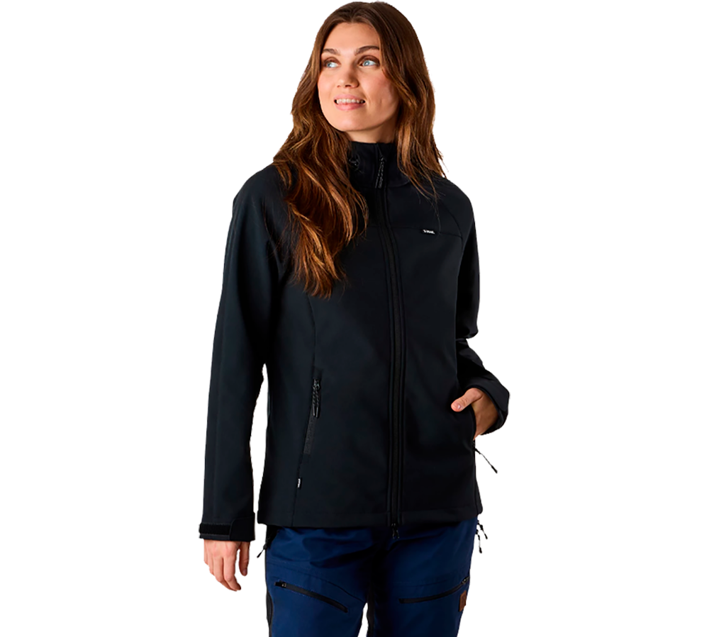 En ung kvinde står afslappet i en mørk, tætsiddende softshell-jakke med lynlås, hævet krave og lommer. Hendes langt, bølget hår falder over skuldrene, og hun kigger blidt mod siden med et roligt smil. Hun bærer mørkeblå arbejdsbukser med lynlås-detaljer, hvilket giver et praktisk og outdoor-inspireret look. Stemningen er funktionel, moderne og klar til udendørs aktiviteter eller daglig brug.
