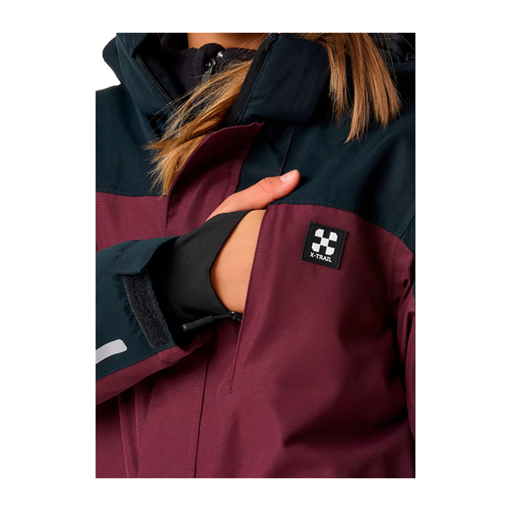 X-TRAIL Cortina Overall Jr er en holdbar og stilfuld børneflyverdragt fra X-Trail. Dragten, der vises her, har en dyb bordeaux og mørkegrøn farvekombination, som giver et moderne og robust udseende. Den er designet til at holde dit barn varmt og tørt i koldt vejr. Med praktiske funktioner som justerbare remme og reflekterende detaljer er denne flyverdragt ideel til vinterens eventyr. En ung pige demonstrerer dragtens pasform og stil, klar til leg i vinterlandskabet.