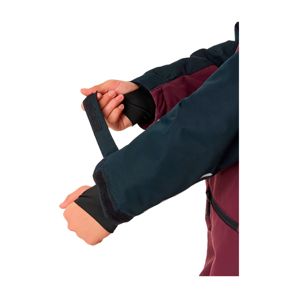 X-TRAIL Cortina Overall Jr er en ideel flyverdragt til børn, hvilket tilbydes af X-Trail. Dragten fremvises her af en ung model, der bærer beklædningsgenstanden i en flot kombination af mørk bordeaux og marineblå. Designet er robust og funktionelt med reflekser på benene for bedre synlighed. Denne dragt er perfekt til udendørsaktiviteter i koldt vejr, og sikrer at barnet holder sig varmt og tørt, mens de nyder vinterens glæder.