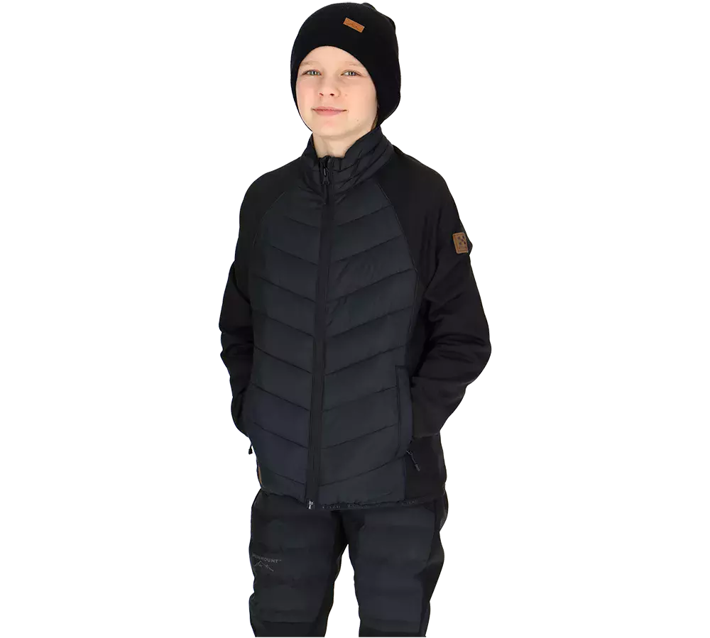 En ung dreng iført en sort vinterjakke med vatterede paneler, sorte bukser og en sort strikhue står afslappet med hænderne i lommerne. Han har et roligt smil og kigger let mod kameraet. Jakken har en høj krave og synlige syninger, mens bukserne virker varme og praktiske. Det ensfarvede, minimalistiske sæt giver et stilrent og funktionelt udtryk til køligere vejr.